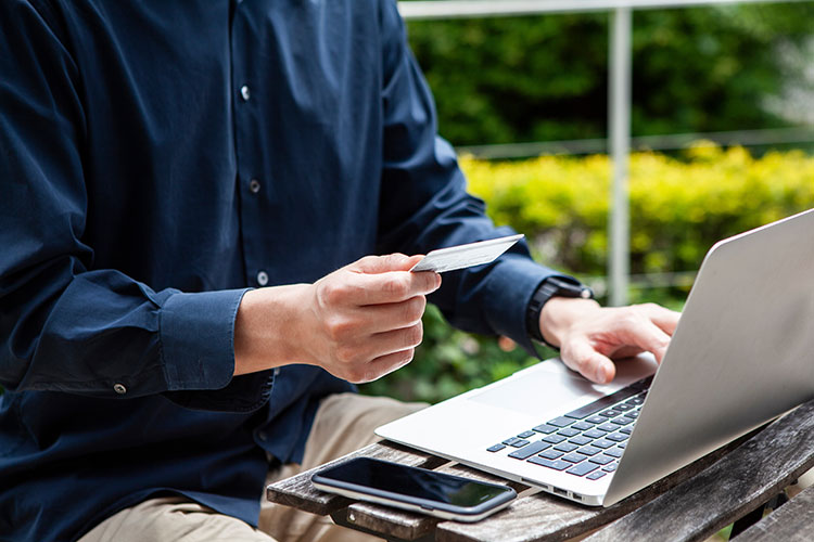 公園でパソコンを開いてクレジット決済をする男性の写真