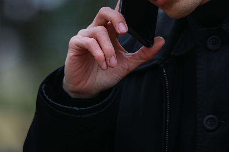外でスマートフォンで会話しているコートを着た男性の写真