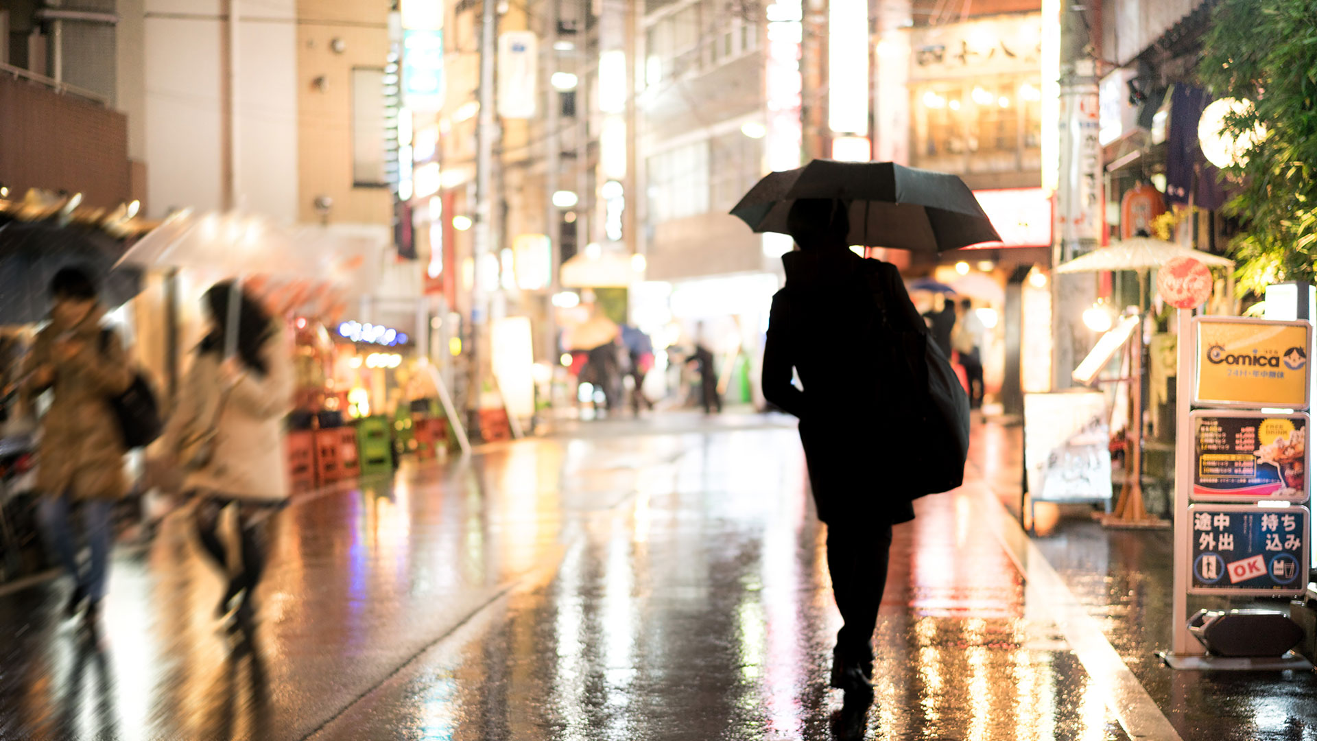 雨の街を傘をさして歩く男性の後ろ姿の写真
