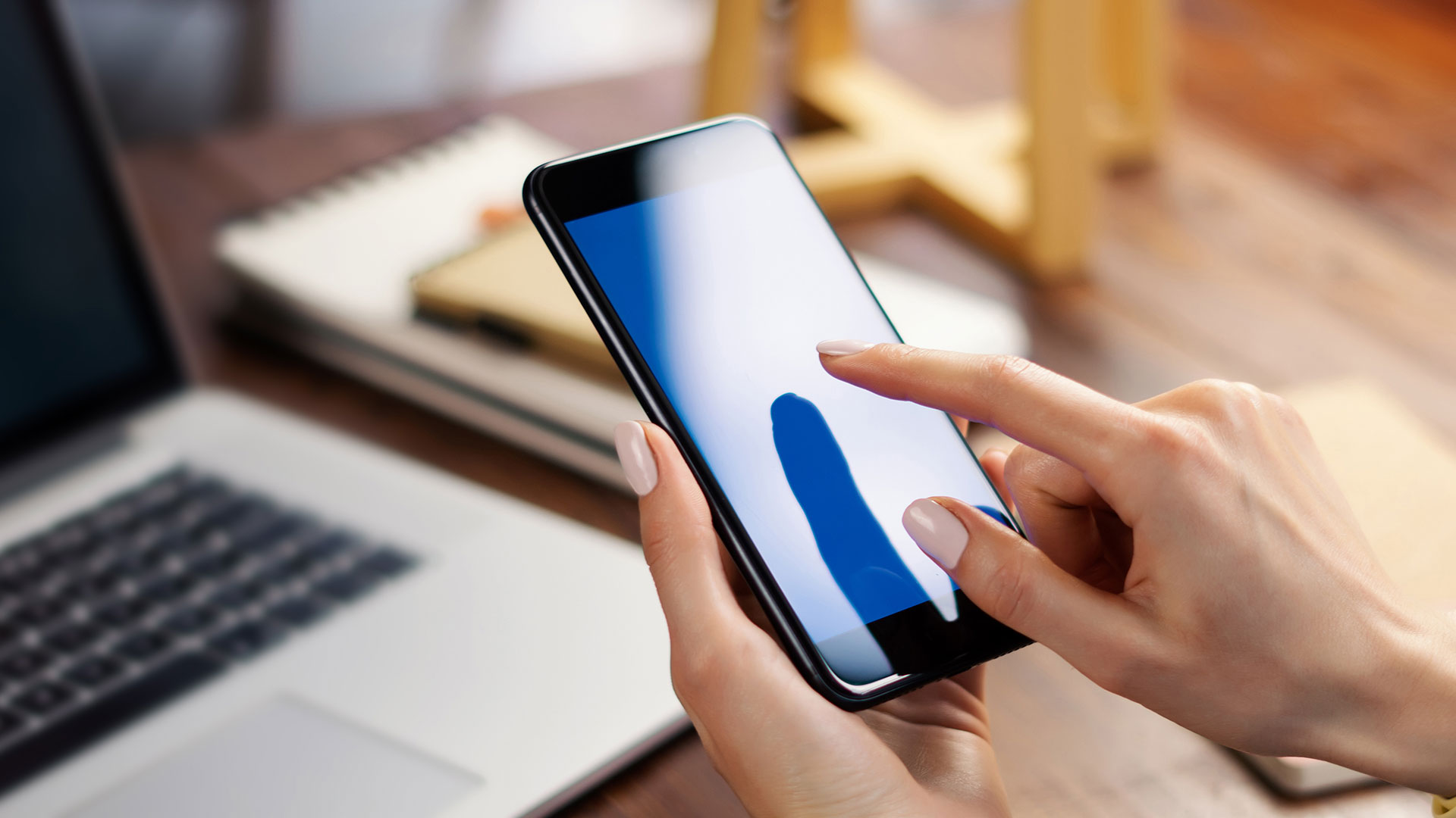 ブック型PCを置いたデスクの前でスマートフォンを操作する女性の手元の写真